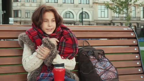 Young Person Sitting on Bench Drinks Thermos