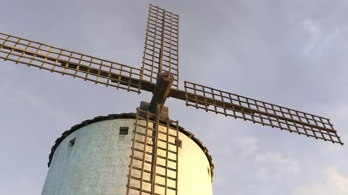 Closeup shot of a vintage Spanish windmill's wings rotating slowly at sunset. 4K