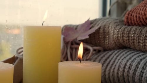 Burning Candles with Stacked Knitted Blankets on Window Sill