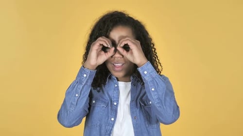 Afrikanisches Mädchen auf der Suche mit handgemachtem Fernglas isoliert auf gelbem Hintergrund