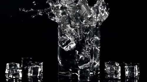 Super Slow Motion Ice Cubes Fall Into a Glass of Water with Spray