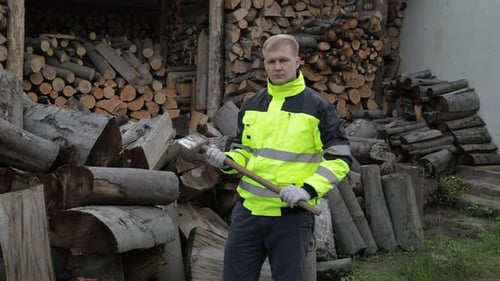 Holzfäller in reflektierender Jacke. Mann Holzfäller mit großer Axt. Gesägte Stämme, Brennholz-Hintergrund