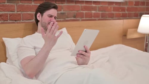 Frustrated Man Using Tablet in Bed