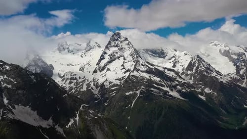 Air Flight Through Mountain Clouds Over Beautiful Snowcapped Peaks of Mountains and Glaciers