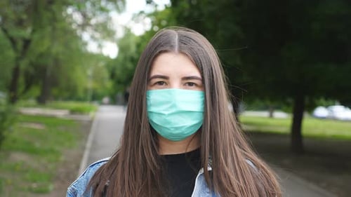 Portrait of Young Woman with Medical Face Mask Stands at City Street. Girl Wearing Protective Mask