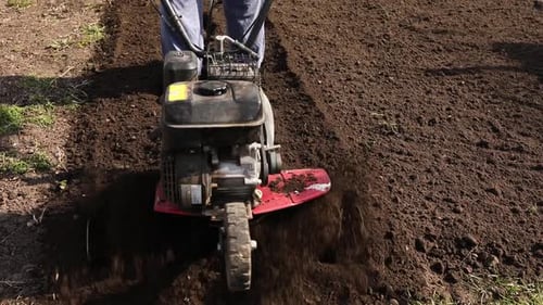 Senior Man Farmer working in the garden plows with Garden Tiller