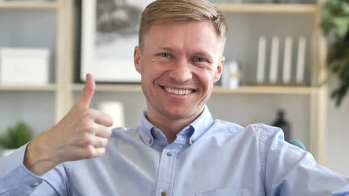 Thumbs Up By Businessman at Work Looking at Camera