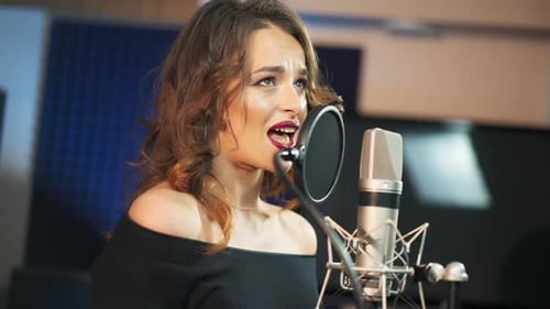 Beautiful woman singing into a large microphone. Professional recording studio.