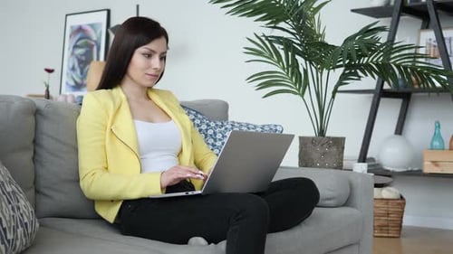 Woman Celebrates Success Using Laptop on Couch