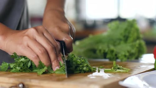Close Up of Hands Chopping Fresh Green Parsley on a Wooden Chopping Board.