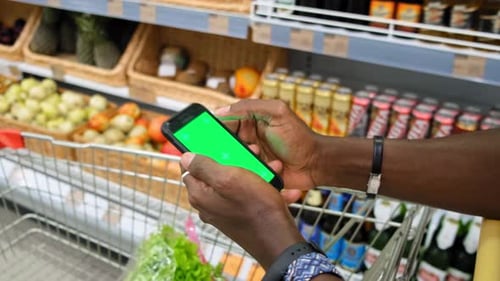 African American Man in a Supermarket with a Green Screen Smartphone Goes Along Fresh Vegetables