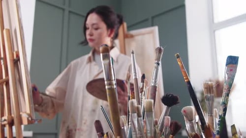 A Woman Artist in a Paintstained Shirt Painting in the Studio By the Easel
