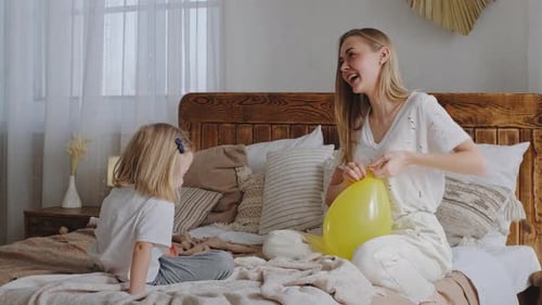 Mother Inflating Balloon With Daughter in Bedroom