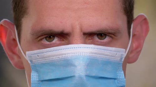 Young Man in a Medical Protective Face Mask Looking at the Camera on the Street Background