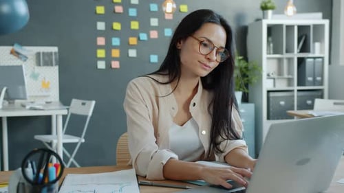 Beautiful Woman Working with Laptop and Writing in Notebook Concentrated on Job in Office