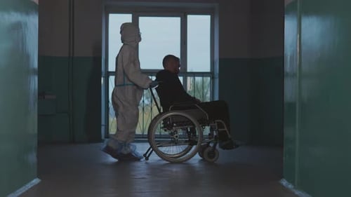 Man in Wheelchair Pushed by Person in Hazmat Suit