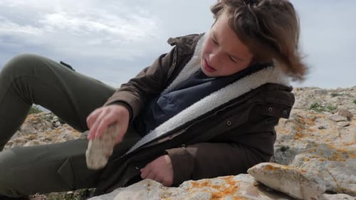 Boy Trying to Break Stone Against Rocky Ground