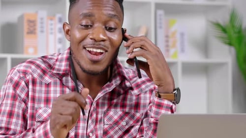 Young Man Talking on Phone While Working on Laptop