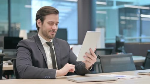 Businessman Browsing Internet on Tablet While Sitting in Office