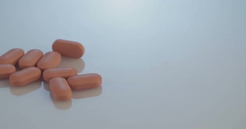 Tan Pills Slowly Slide Into Frame on White Surface