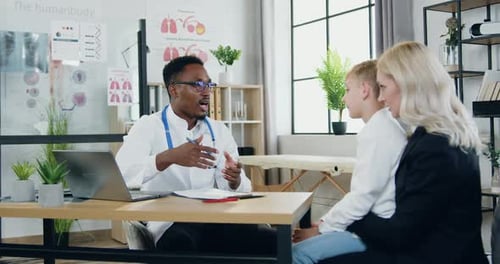 Woman and Her Nice Teen Son Visiting African American Skilled Male Doctor in Modern Medical center