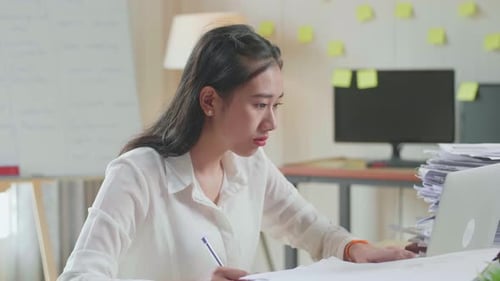 Close Up Of Asian Woman Looking At Laptop And Taking Note While Working With Documents At The Office