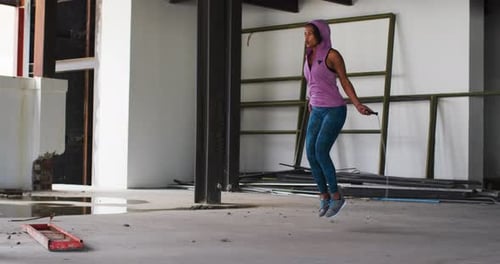 African american woman wearing hoodie skipping with rope in an empty urban building