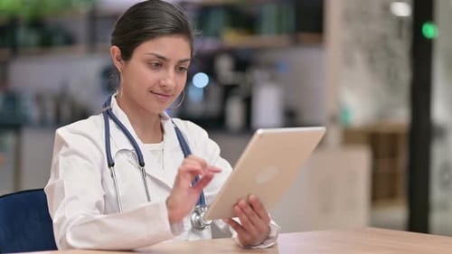 Serious Professional Indian Female Doctor Using Tablet in Cafe
