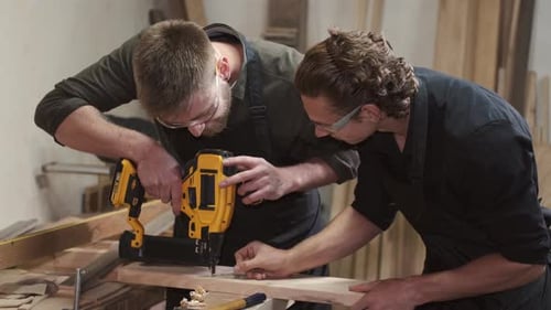 Carpenters with Drill Drilling Plank at Workshop