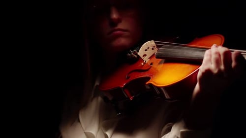 Woman with Glasses Bow Plays the Violin Standing in a Dark Studio