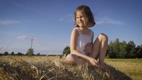 Cute Little Girl Sits on Mown Rye in the Field
