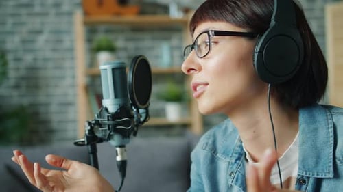 Close-up of Young Lady in Headphones Speaking in Microphone Smiling in Studio