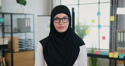 Arabische Geschäftsfrau im Hijab blickt vor dem Hintergrund eines modernen Büroraums in die Kamera