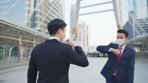 Asian business people wearing protective face mask making elbow touch to avoid coronavirus in city.