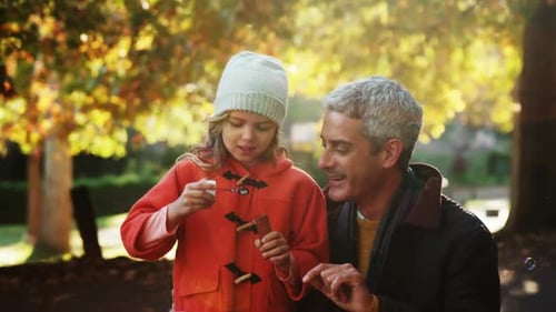 Girl Blowing Bubbles with Her Father in Park