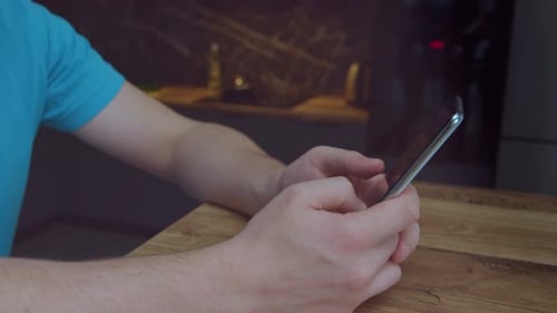 Mann mit einem Handy in der Hand, der an einem Holztisch sitzt, nutzt eine App Home Office