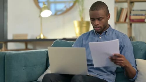 Man Working on Laptop with Paperwork at Home