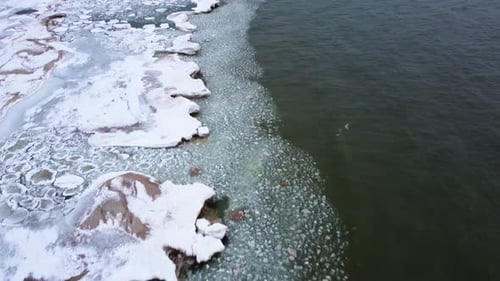 4K Drone video of frozen lakeshore with the camera panning up to reveal the sand dunes