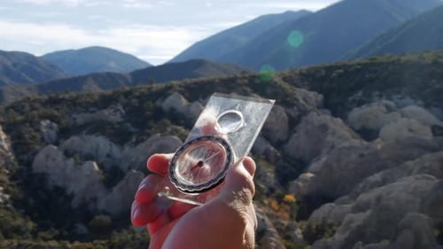 A hikers hand holding a survival compass to find their way back camp safely in a survival situation