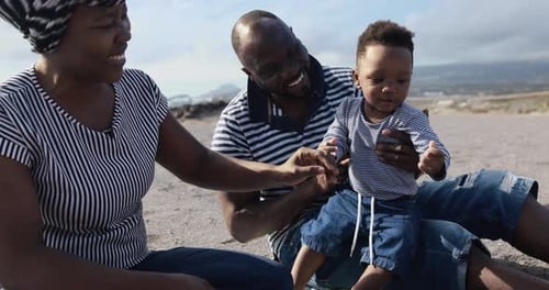 African couple sitting on the beach and having playful time with little son