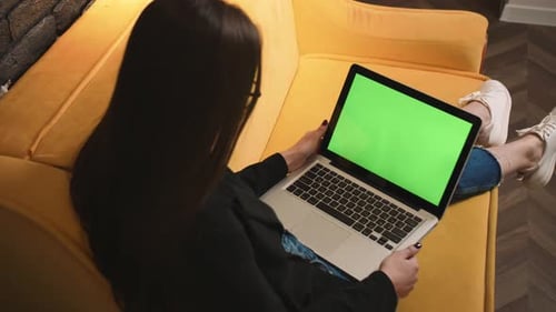 Young Woman Using Laptop with Green Screen Lying on the Couch Sofa at the Home
