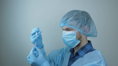 Man in protective medical gear filling syringe with drugs for virus infection prevention.