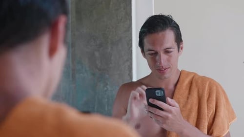 Young Man Using Smartphone in Bathroom Mirror