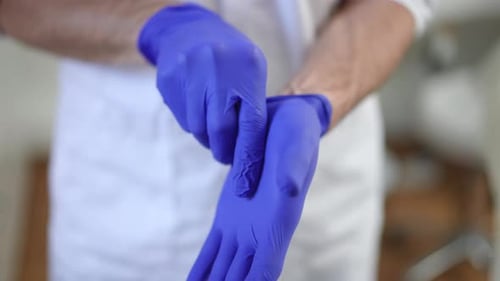 Male Surgeon Putting on Blue Medical Gloves Standing in Hospital Indoors