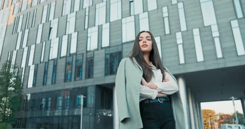 Pretty Women with Magnificent Figure Stands in Front of Modern Office Building Dressed in Elegant