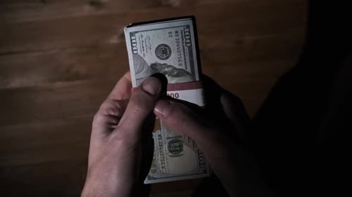 Hands Hold Stacks of Money in Dark Setting