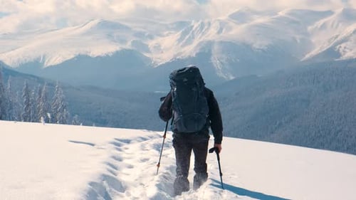 Man Backpacker Hiking Snowy Mountain Hillside on Cold Winter Day