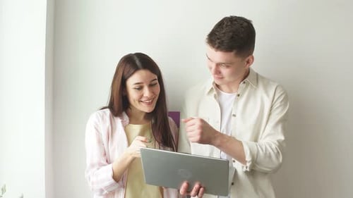 Zwei fröhliche positive Profis schauen auf einen Laptop-Bildschirm.