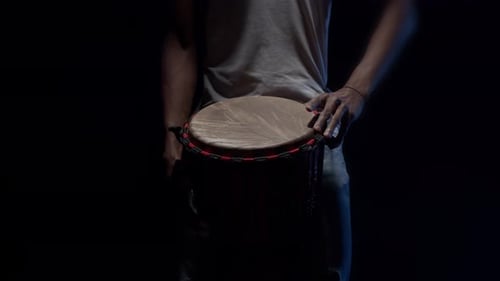 Un batteur noir joue avec les mains sur un tambour africain dans le studio dans le noir