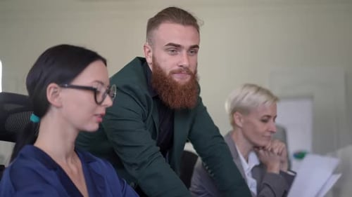 Confident Bearded Caucasian Man in Formal Suit Talking with Female Colleagues Sitting at Table